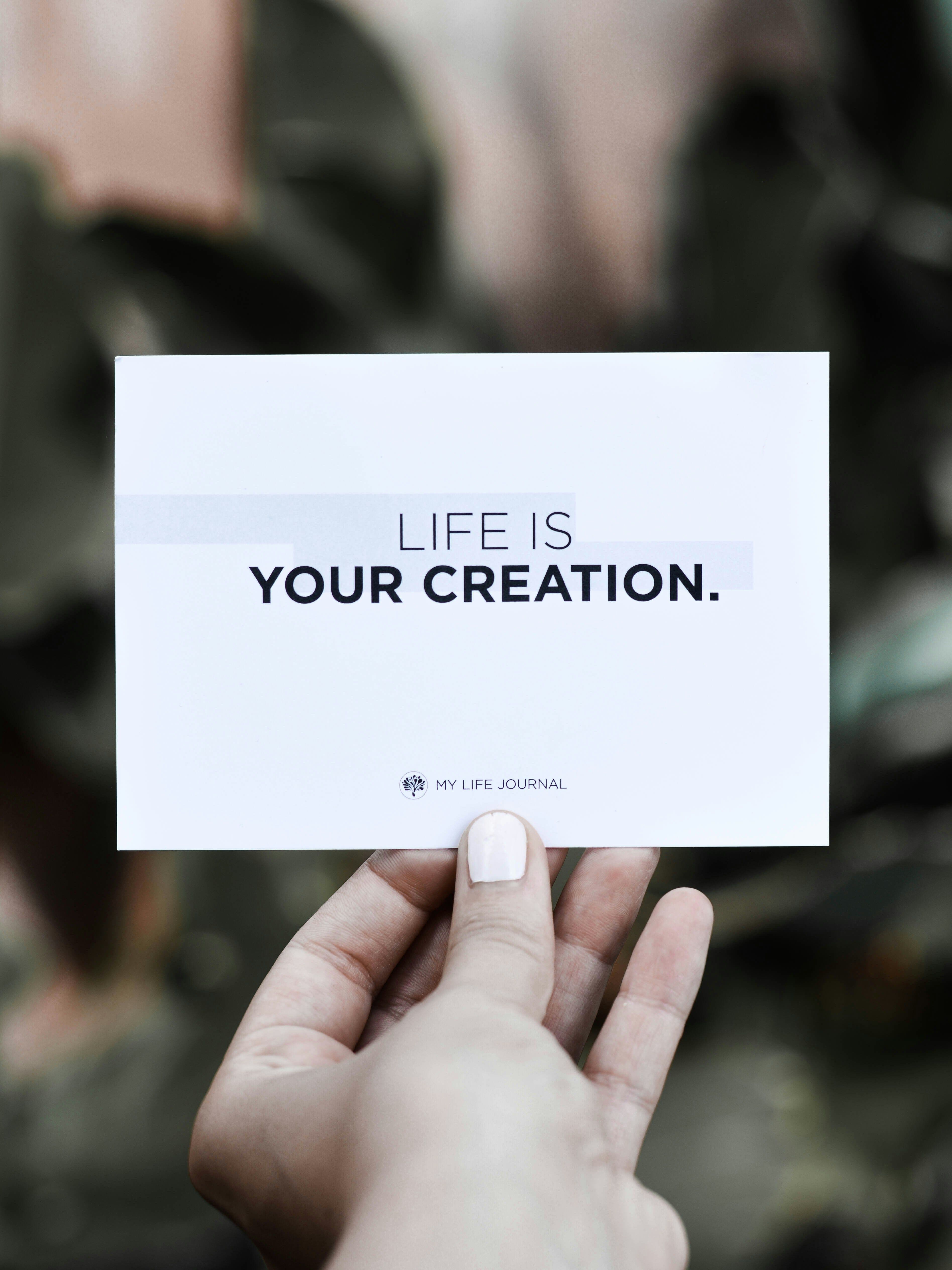 Χέρι που κρατά κάρτα με τη φράση «Life is your creation», σύμβολο αυτογνωσίας, αλλαγής νοοτροπίας και προσωπικής ανάπτυξης μέσα από coaching.